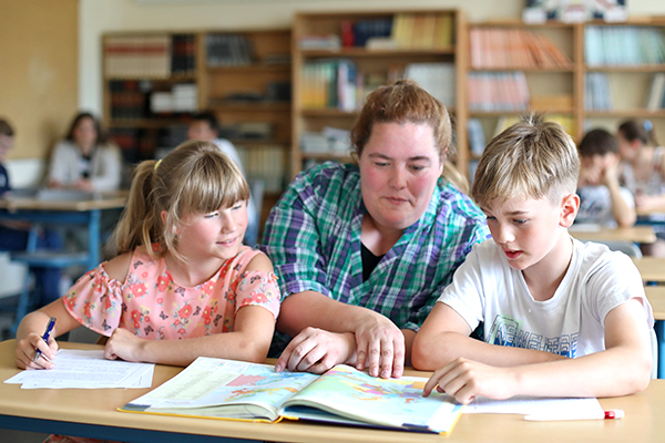 Pädagogische Fachkraft schaut mit Kindern in ein Lehrbuch, Foto: Danny Gohlke an der Baltic-Schule Rostock