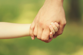 Die Hand eines erwachsenen Menschen hält die Hand eines Kindes vor einem verschwommenen grünen Hintergrund