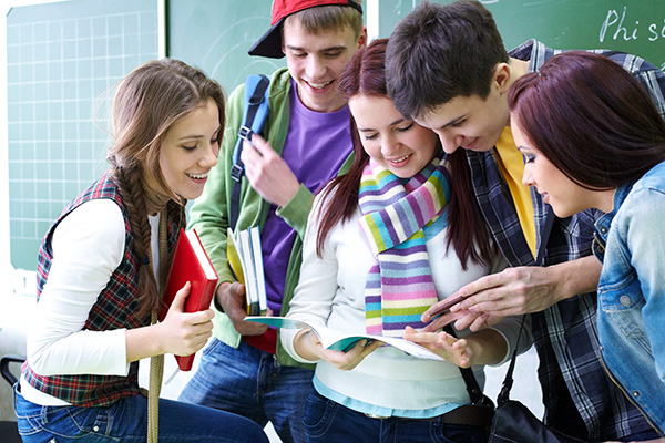 Eine Gruppe von Schülerinnen und Schüler steht vor der Tafel im Klassenraum und freut sich über gute Noten. Foto: yanlev/colourbox.com