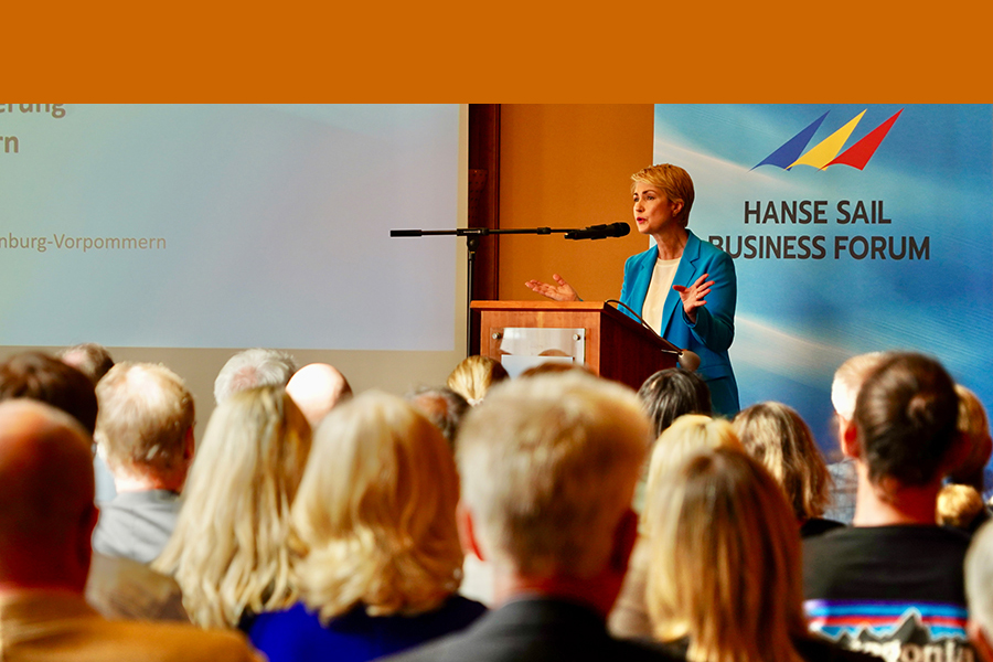 Ministerpräsidentin Manuela Schwesig am Redepult mit Mikrophon beim Hanse Sail Business Forum mit einer Geste. Von hinten sind einige Besucherinnen und Besucher des Forums zu sehen.