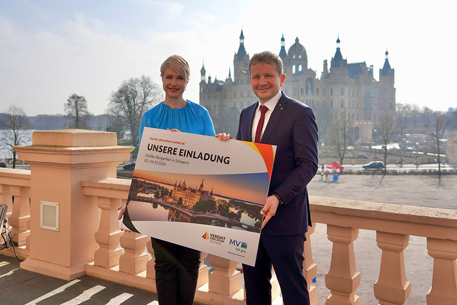 Ministerpräsidentin Manuela Schwesig und Schwerins Oberbürgermeister Dr. Rico Badenschier präsentieren gemeinsam ihre Einladung zum großen Bürgerfest auf dem Tag der Deutschen Einheit in Schwerin. Im Hintergrund ist das Schweriner Schloss zu sehen.