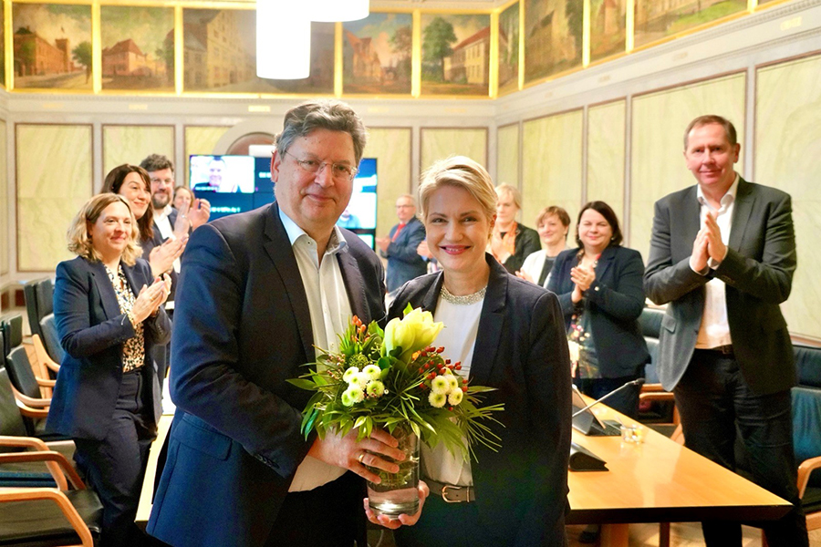 Ministerpräsidentin Manuela Schwesig steht mit Minister Reinhard Meyer, der einen Strauß in den Händen hält, vor dem Kabinettstisch. Im Hintergrund applaudieren die Kabinettsmitglieder.